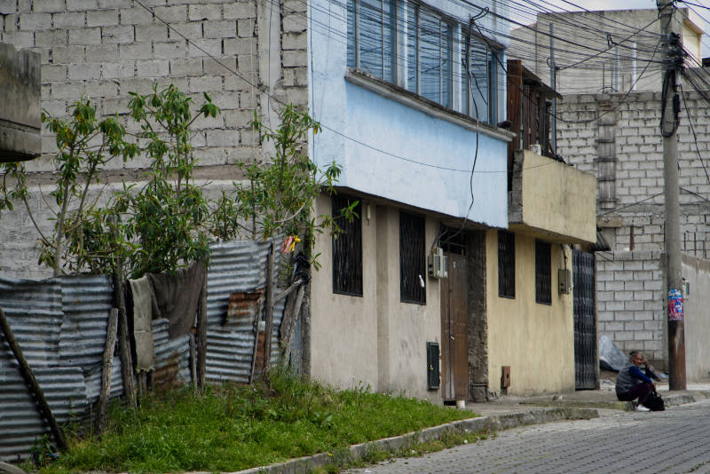 @laguachimania-calle-sur-de-quito-cerramiento-de-zing Calle del sur de Quito una mujer espera sentada junto a un poste de energía eléctrica